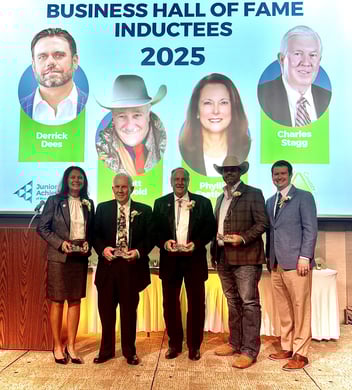 Business Hall of Fame inductees accepting awards on stage with smiling portraits behind them.